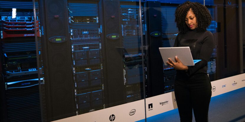 A female engineer using a laptop while monitoring data servers in a modern server room.