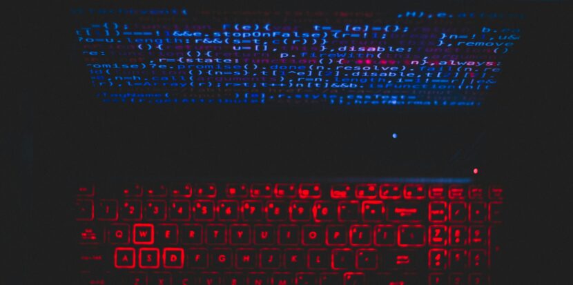 Dark-themed laptop setup with a red glowing keyboard and code on screen, ideal for tech enthusiasts.
