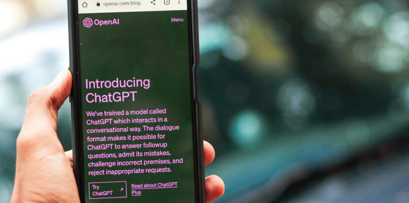 Close-up of a smartphone showing ChatGPT details on the OpenAI website, held by a person.